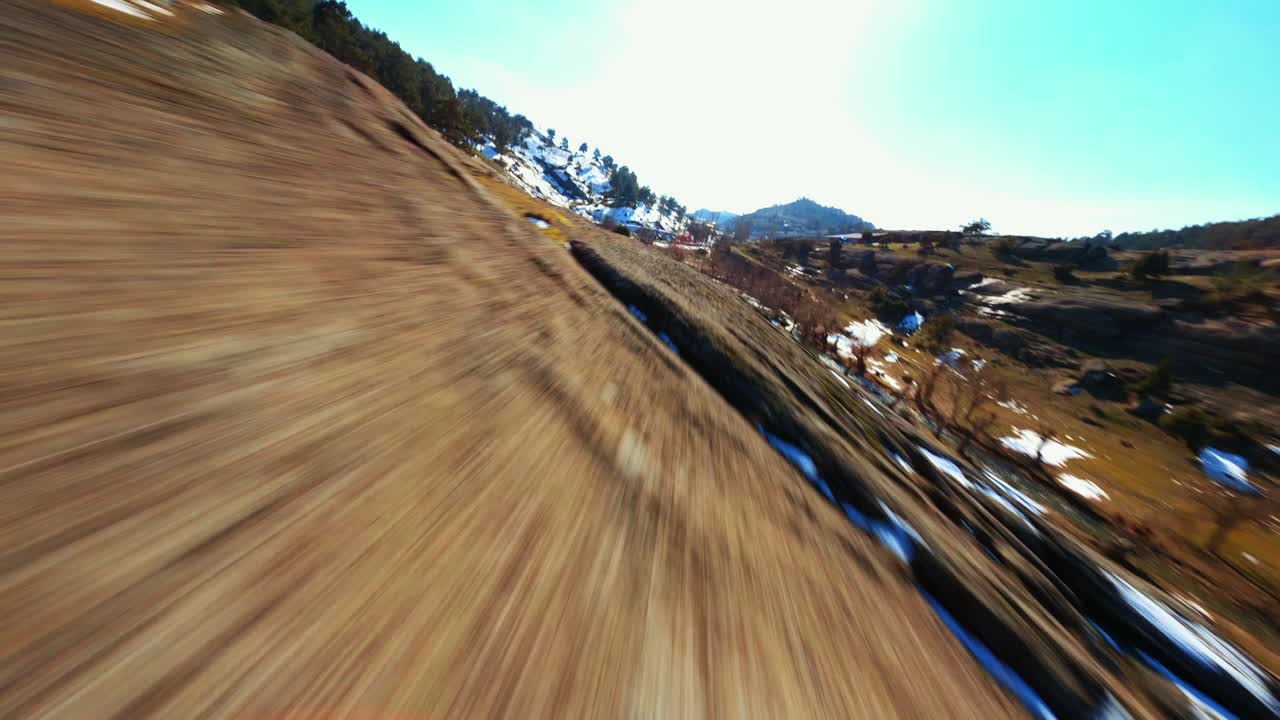 4k fpv 드론이 바위산 옆으로 날아다니고, 나무가 있는 땅의 눈과 흙