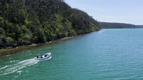 A-stunning-total-view-tracking-shot-of-a-small-boat-on-the-Australian-coast,-sunny-day,-trees,-sea,-and-daylight