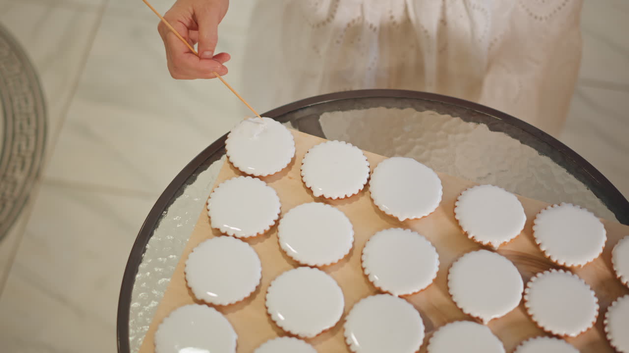 Overhead view mini pumpkin pies on glass table caucasian chef uses wooden skewer to lift single pie careful placement product styling muted palette tile floor backdrop methodical packaging prep modern