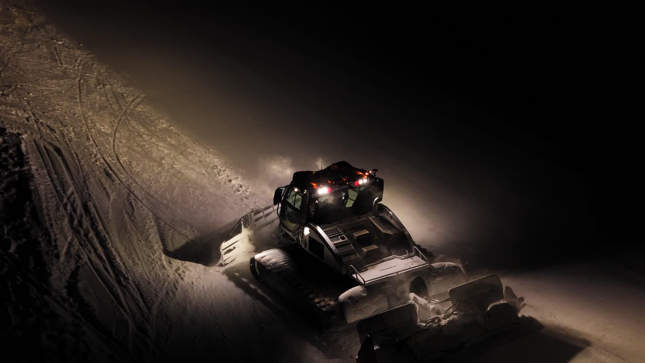 Bulldozer che sgombera la neve di notte nelle Dolomiti, Italia, con luci intense e raffiche nevose.