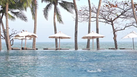 Canvas-sun-umbrellas-are-lined-up-along-the-edge-of-a-swimming-pool