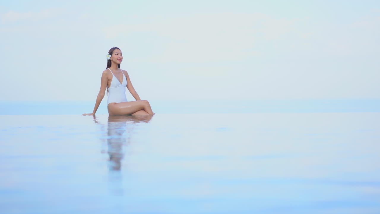 вдалеке симпатичная молодая женщина в купальном костюме плавает на краю бассейна