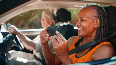 Passagier-Fotografiert-Mit-Dem-Handy,-Während-Zwei-ältere-Freundinnen-Einen-Tagesausflug-Im-Auto-Genießen