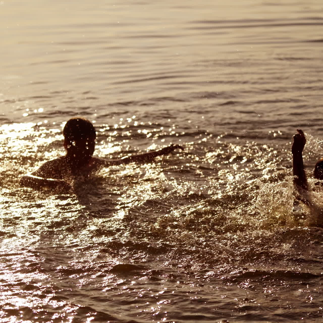 Joyful children playing with water at sunset. Young boys having fun in the river. Two brothers splashing in water in the evening.