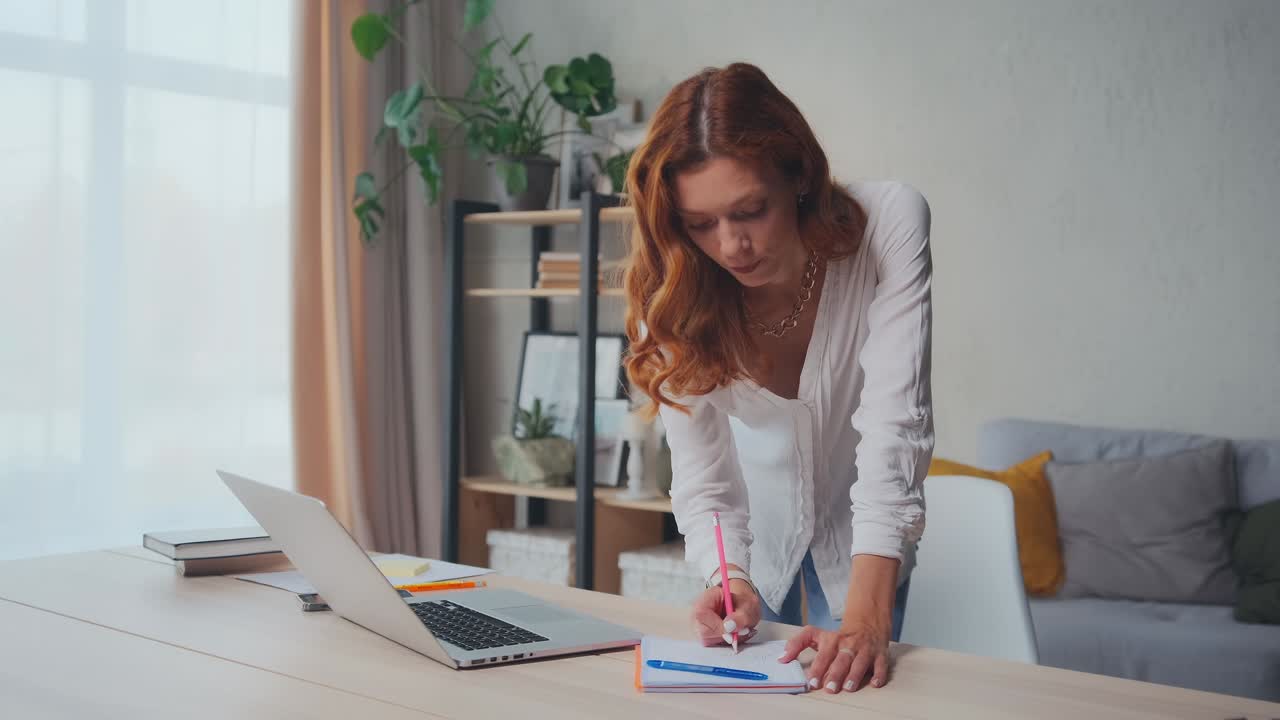 Caucasian student woman taking notes in notebook from laptop