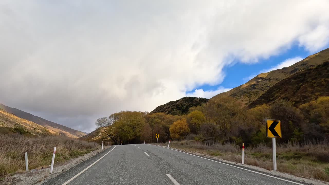 A tranquil drive through Wanaka's winding roads, surrounded by lush hills and dynamic skies, captured in natural daylight