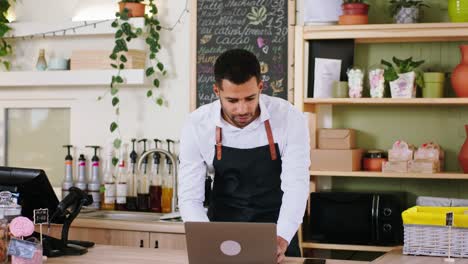 concepto de pequeña empresa y empresario barista carismático chico usando el teléfono inteligente para tomar un pedido en línea y escribir en la computadora portátil en la acogedora cafetería