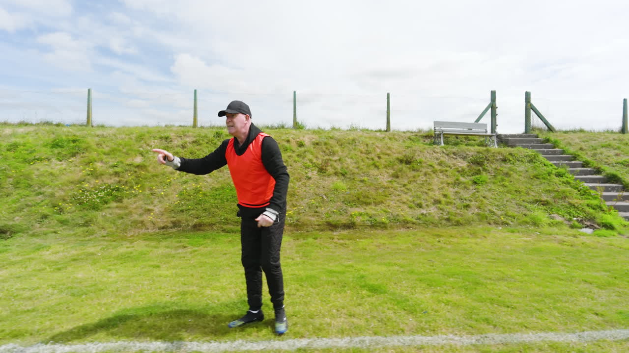 Male coach walking, giving instructions and observing soccer game on pitch