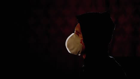 silhouette of man in hood and medical mask watching tv with fake news. pandemic