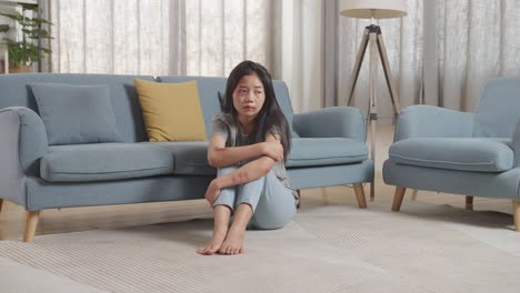 full body of young asian woman victim of violence with bruise on body sits hugging her knees being sad from physically abused at home