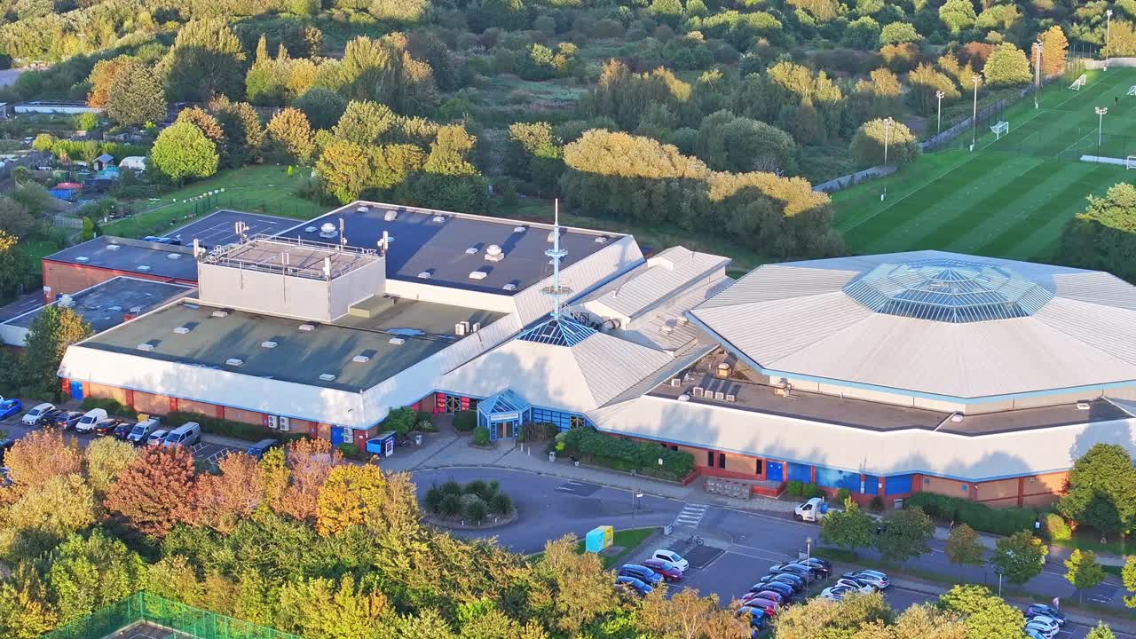 황금 시간 의 빛 의 광선 이 기하학적 인 건물 들 을 가로질러 퍼지면서 나무 들 사이 에 있는 학교 위 에 올라간다