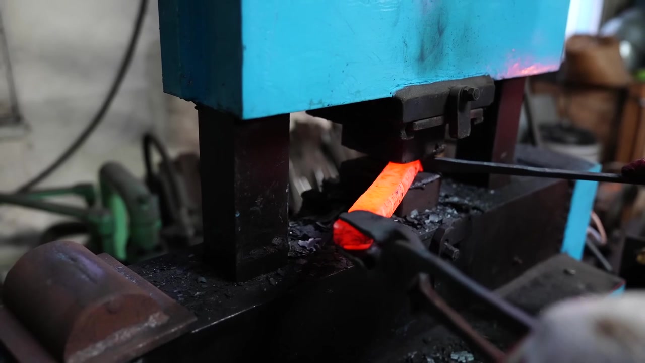 Long orange hot steel bar compressed and elongated under a mechanical forging hammer in a Korean smithy