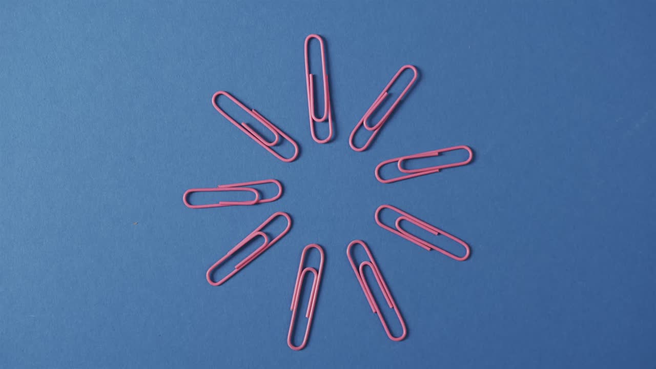 Overhead view of pink paper clips arranged on blue background, in slow motion