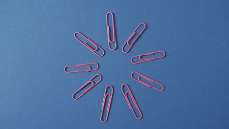 overhead view of pink paper clips arranged on blue background, in slow motion