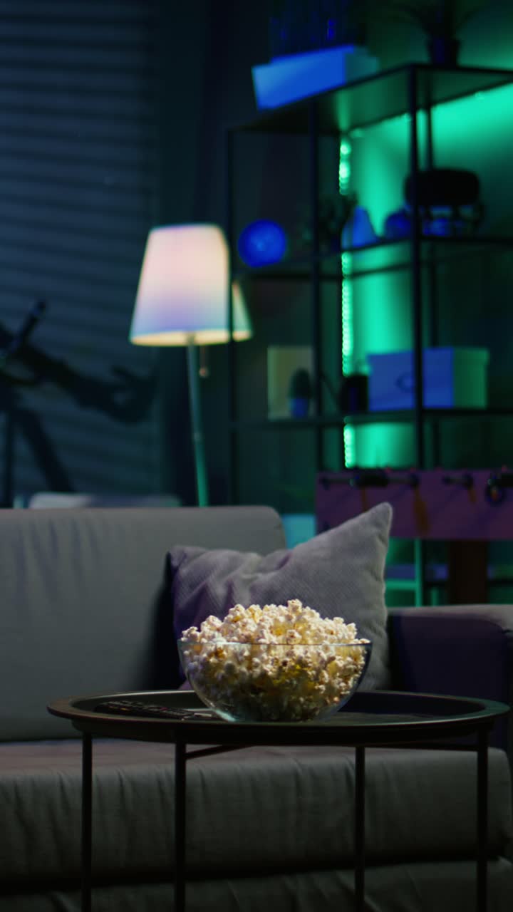 Vertical video Bowl of popcorn on table in neon illuminated home theater apartment