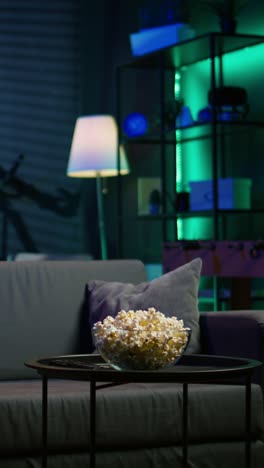 vertical video bowl of popcorn on table in neon illuminated home theater apartment