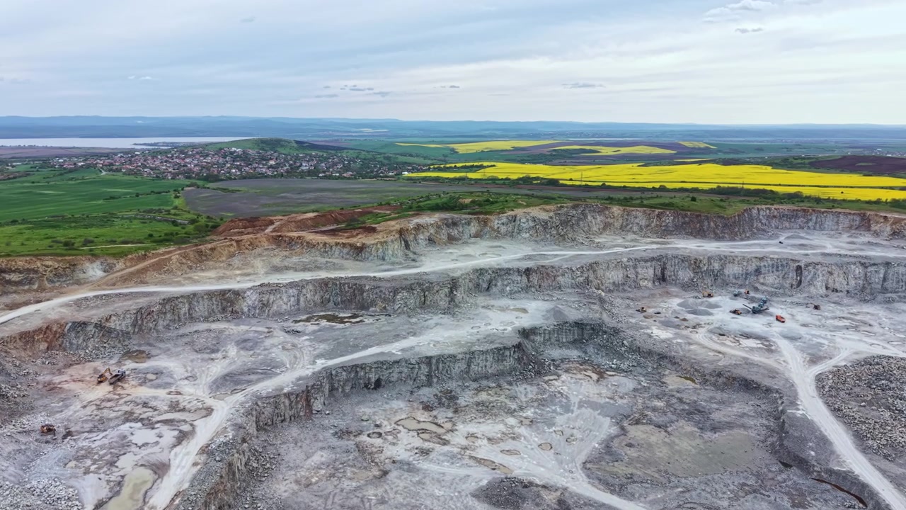 Grande cava vista dall'alto che mostra rocce e macchinari con campi verdi e un orizzonte lontano durante il giorno