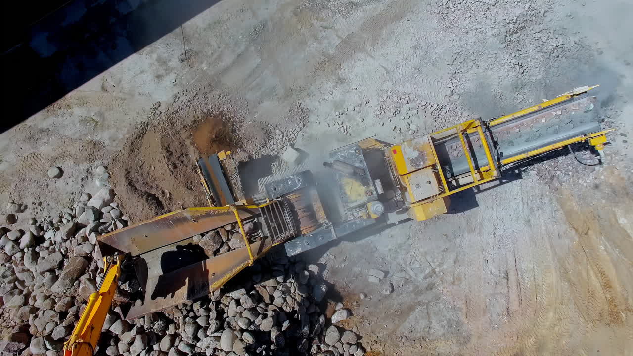 excavadora cargando rocas grandes en una trituradora de piedra para hacer grava - vista aérea giratoria