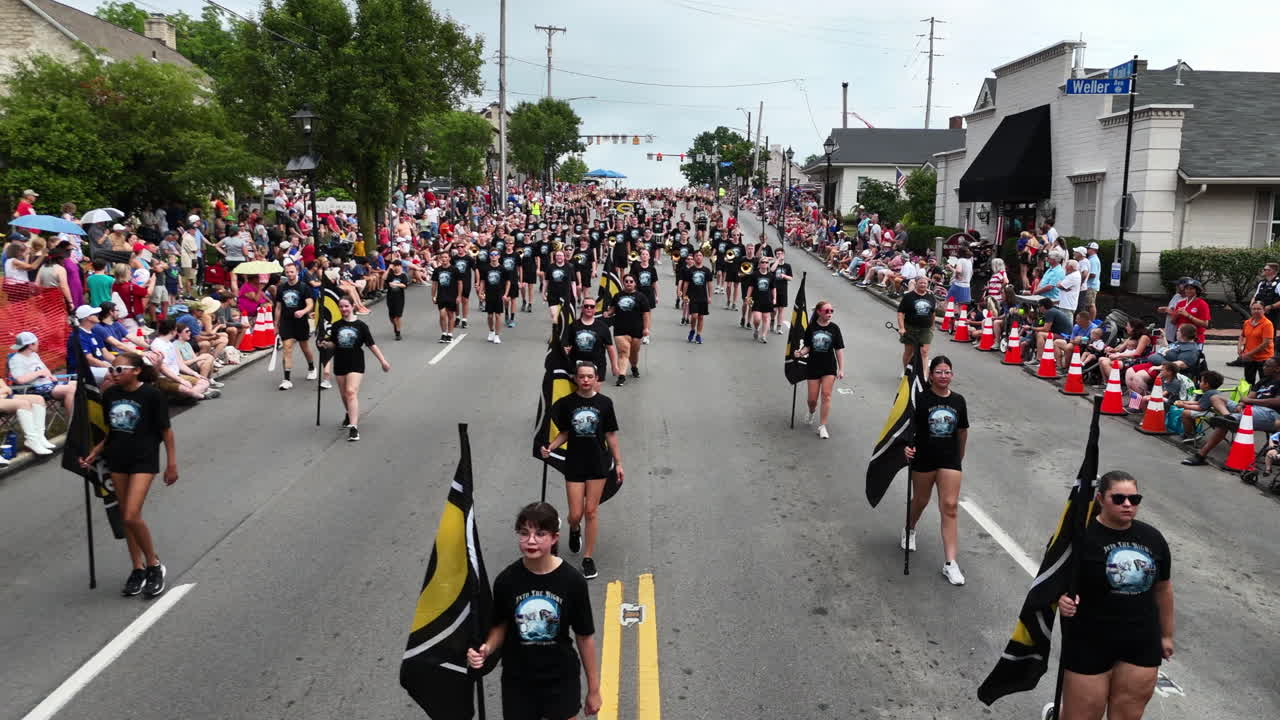 Aerial dolly above high school marching band carrying instruments and banners in parade for independence day parade
