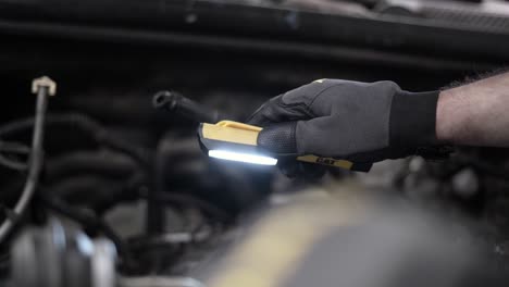 low-angle shot of a mechanic using a light to check in a car engine bay