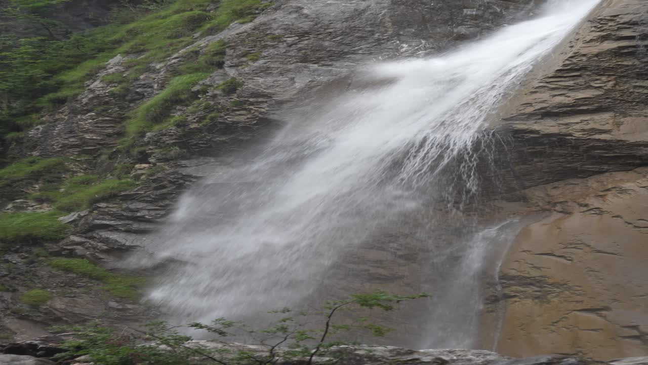 Klöntal waterfall drops over rocky cliff in Glarus Switzerland with mist rising from strong alpine water flow