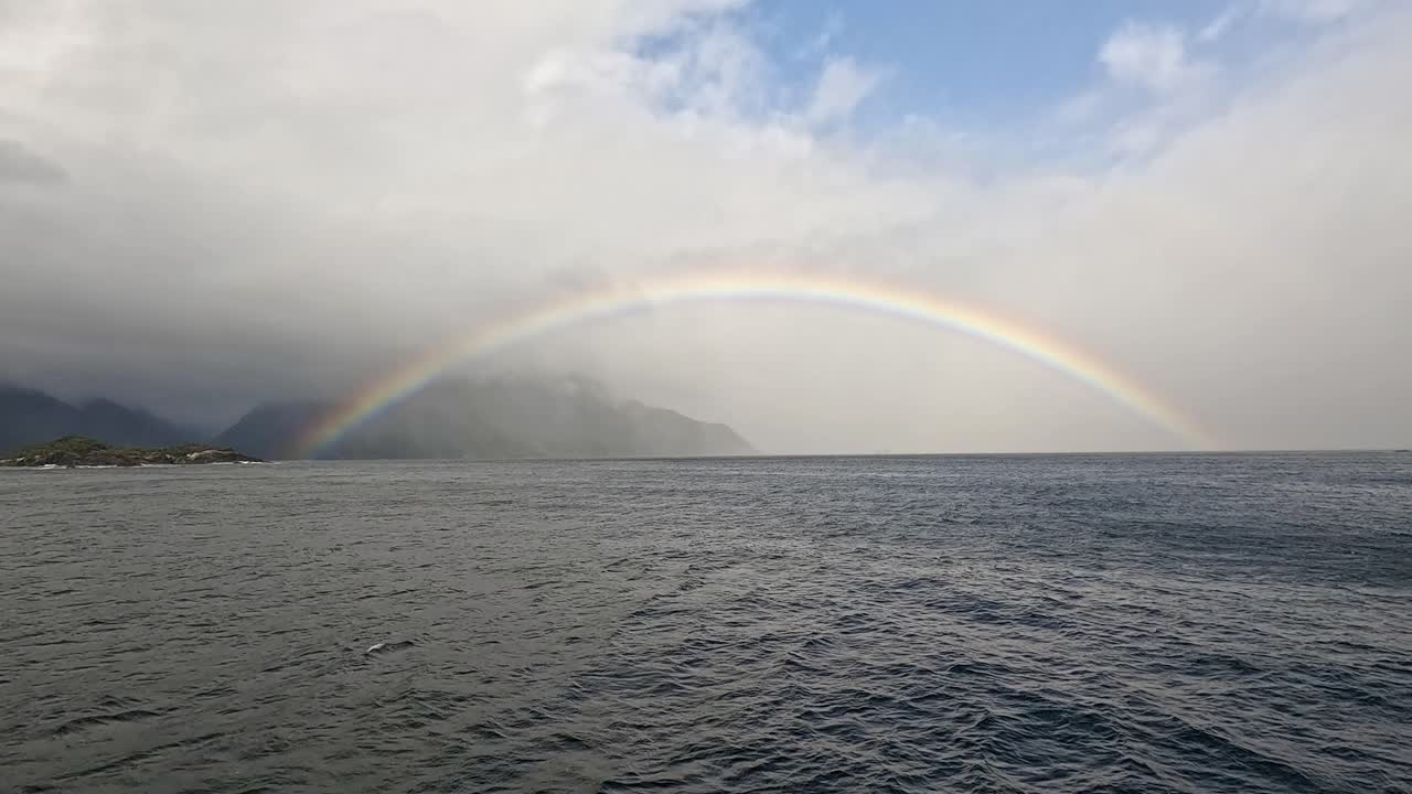 View of a rainbow while sailing Doubtful Sound in the Fiordland National Park in New Zealand's South Island. You can see the mist in the distance and clouds in the sky