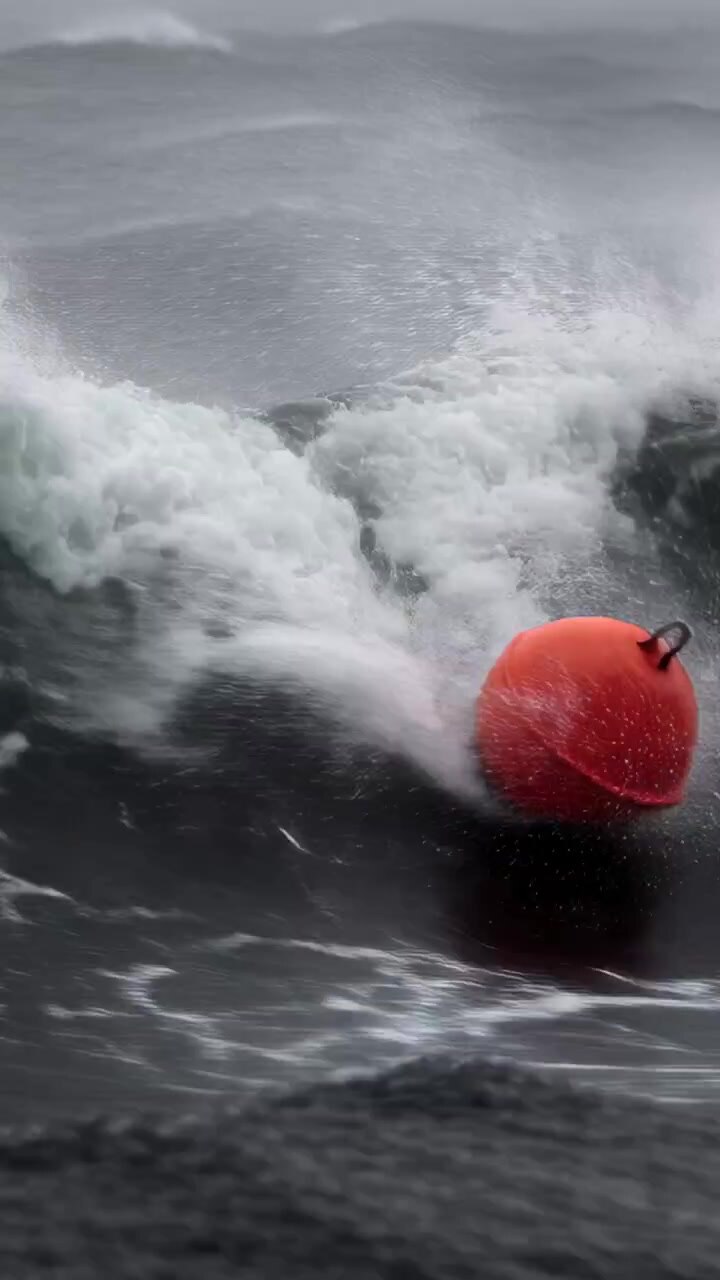 Vertical video: Red buoy getting hit by breaker, rolling into trough at sea, eyelet showing