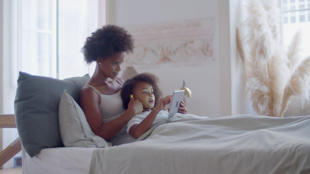 madre afroamericana e hija acostadas en la cama y relajadas