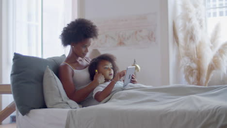 african american mother and daughter lying in bed and relaxing