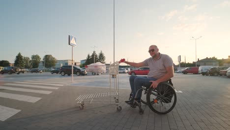 man with disabilities in wheelchair pushing cart in front of himself at supermarket parking