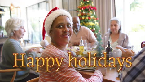 animation of happy holidays text over diverse senior friends at christmas dinner at home