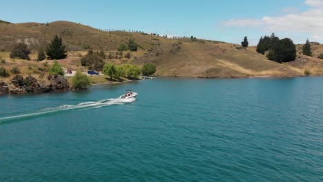 Cámara-Lenta---Antena---Barco-En-El-Lago-Dunstan,-Otago-Central,-Nueva-Zelanda-Con-Montañas-Y-Nubes-En-El-Fondo