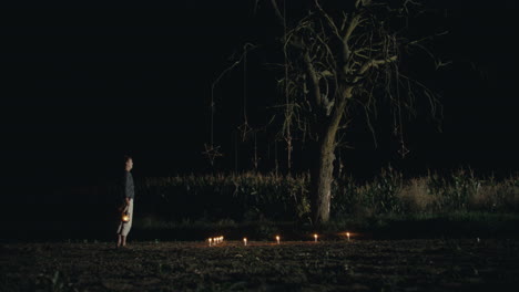 a solitary night ritual under a bare tree