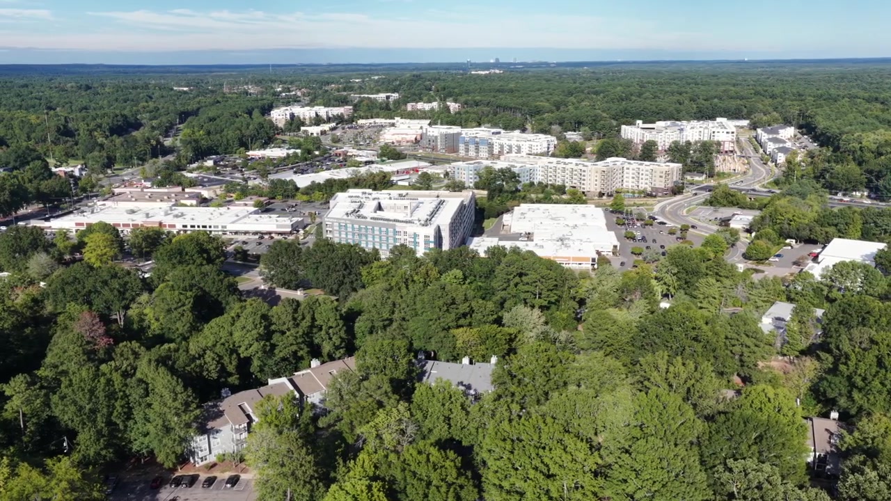 Uno sviluppo a uso misto di negozi, uffici e appartamenti si estende attraverso la foresta vicino alla Duke University a Durham, nella Carolina del Nord, con le torri degli uffici in lontananza sullo skyline. Vista aerea