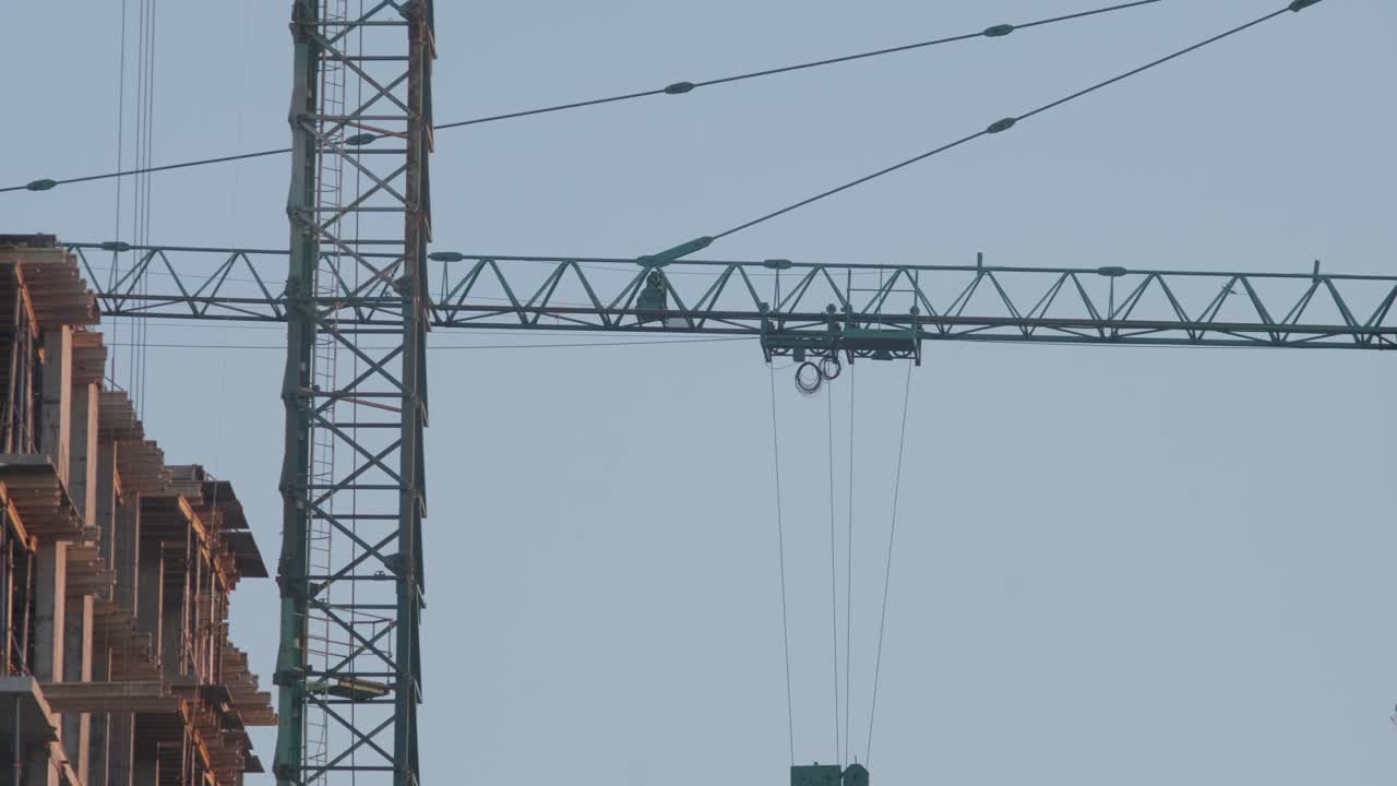 vista de cerca de una gran grúa de construcción verde que se alza contra un cielo azul claro, destacando el brazo de la grúa, la cabina del operador y el intrincado sistema de cables