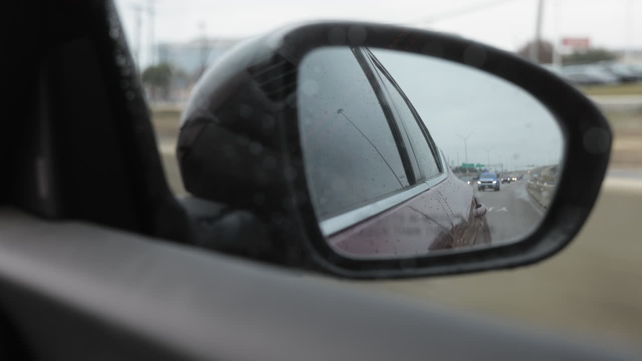 POV looking in to the passenger rearview mirror in a modern sedan on a frontage road to a highway