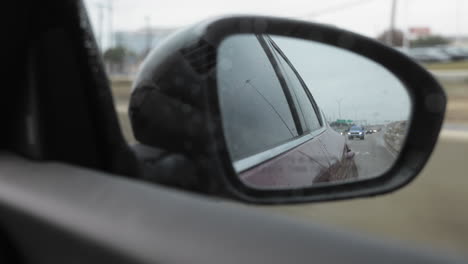 pov looking in to the passenger rearview mirror in a modern sedan on a frontage road to a highway