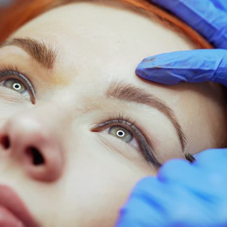 hands of the master are putting a tattoo on the edge of the eyebrow for a pretty woman in a beauty salon. cosmetology. close-up