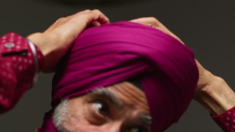 close up low key studio lighting shot of senior sikh man with beard tying fabric for turban against dark background 2