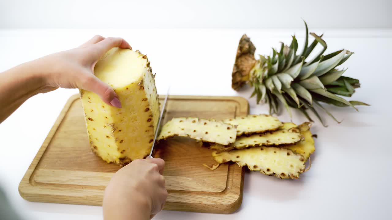Peeling pineapple on a cutting board. Female's hands cleaning fresh exotic fruit with a knife. Tropical food.