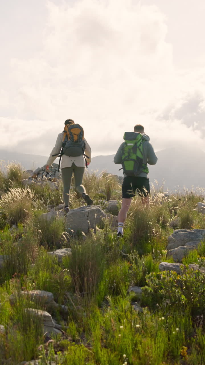 Coppia che fa un'escursione in salita su un sentiero di montagna roccioso con zaini.