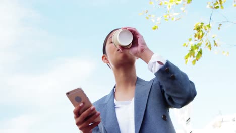 woman sipping coffee outside and using smartphone