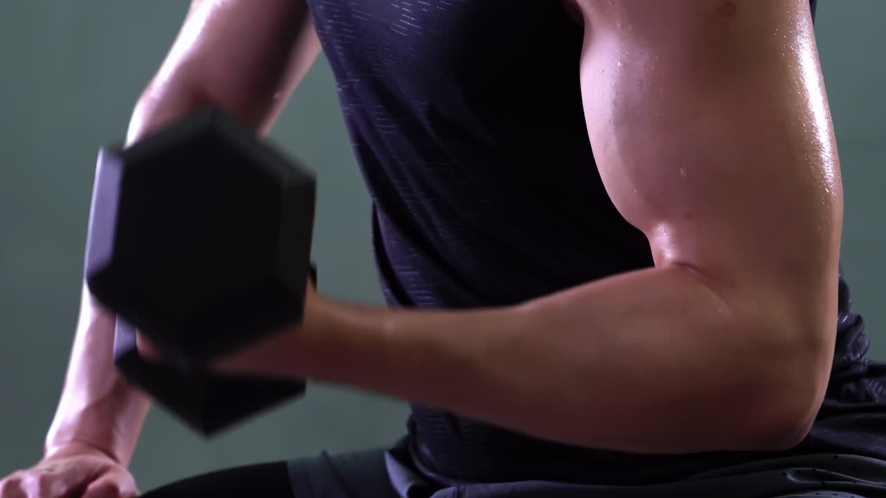 Young sportsman holds dumbbell in hand and does exercises for arm muscles, pumping up biceps at home in daytime. Sports equipment for home training.