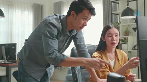 asian female has discussion with male while work on computer in the office