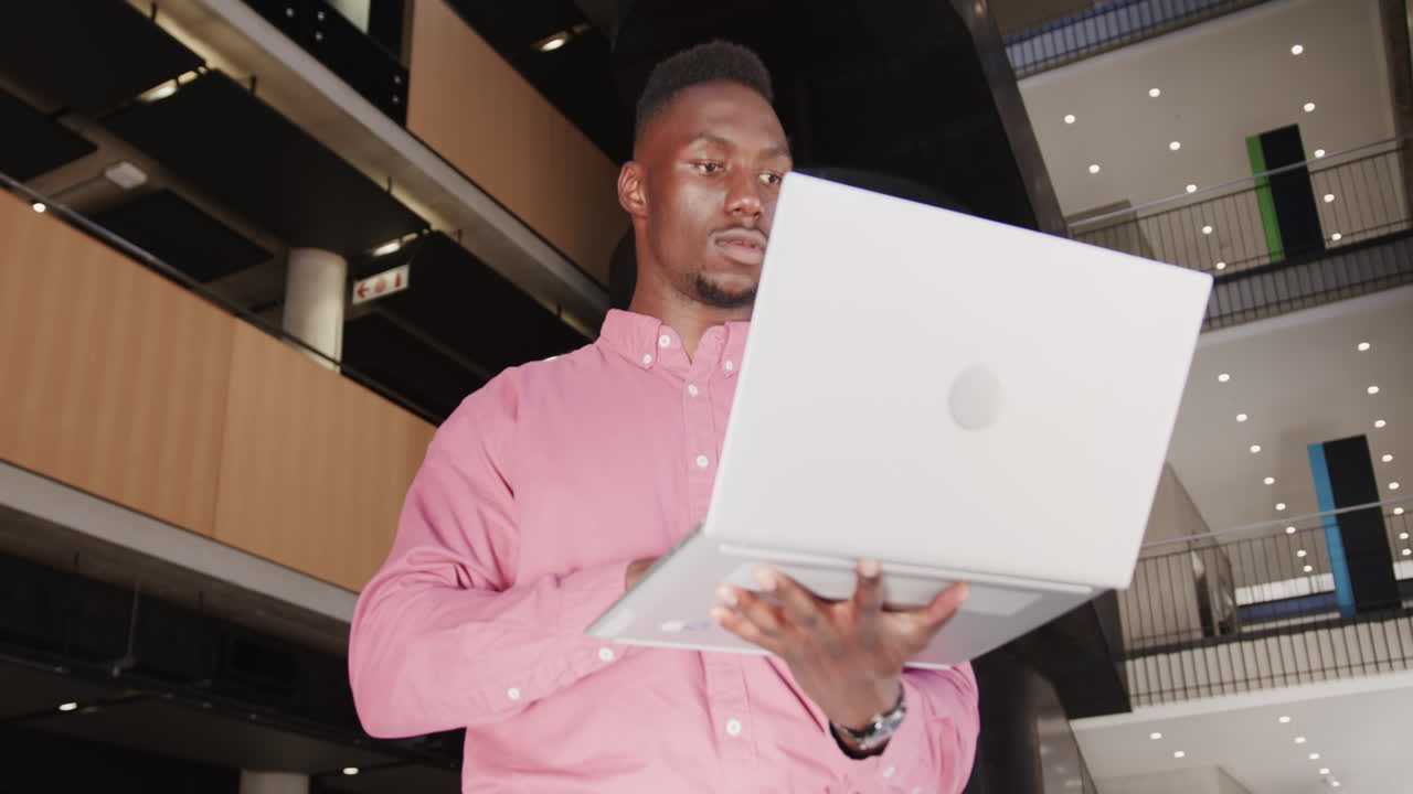 Holding laptop, businessman in pink shirt working in modern office building