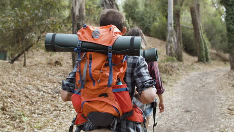 couple of hikers with camping backpacks walking on forest path