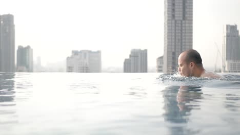 Piscina-Infinita-Con-El-Fondo-Del-Edificio-De-Rascacielos-De-La-Ciudad-Mientras-Se-Pone-El-Sol,-Destino-De-Vacaciones-De-Verano,-Complejo-Hotelero-De-La-Ciudad