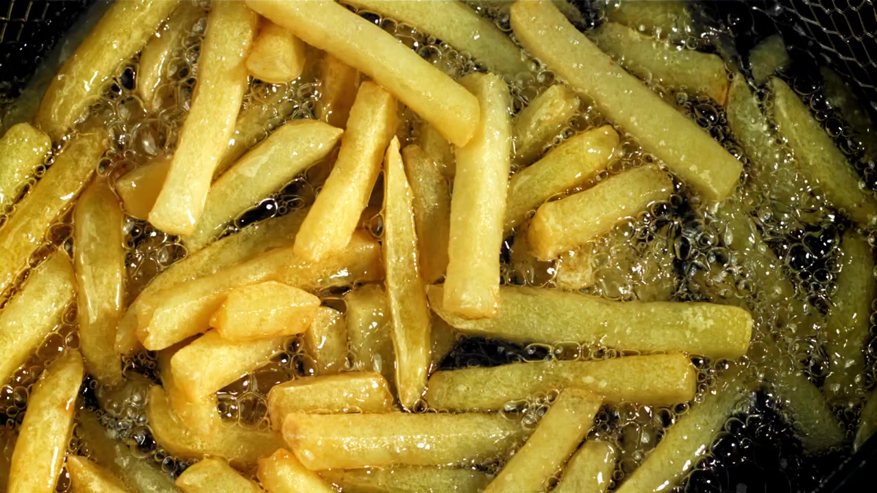 Patatas fritas doradas friéndose en aceite caliente, primer plano