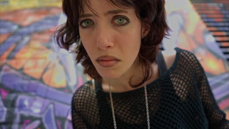 outdoor fashion portrait of young alternative style woman leaning in towards camera against graffiti covered walls of london city street uk in real time