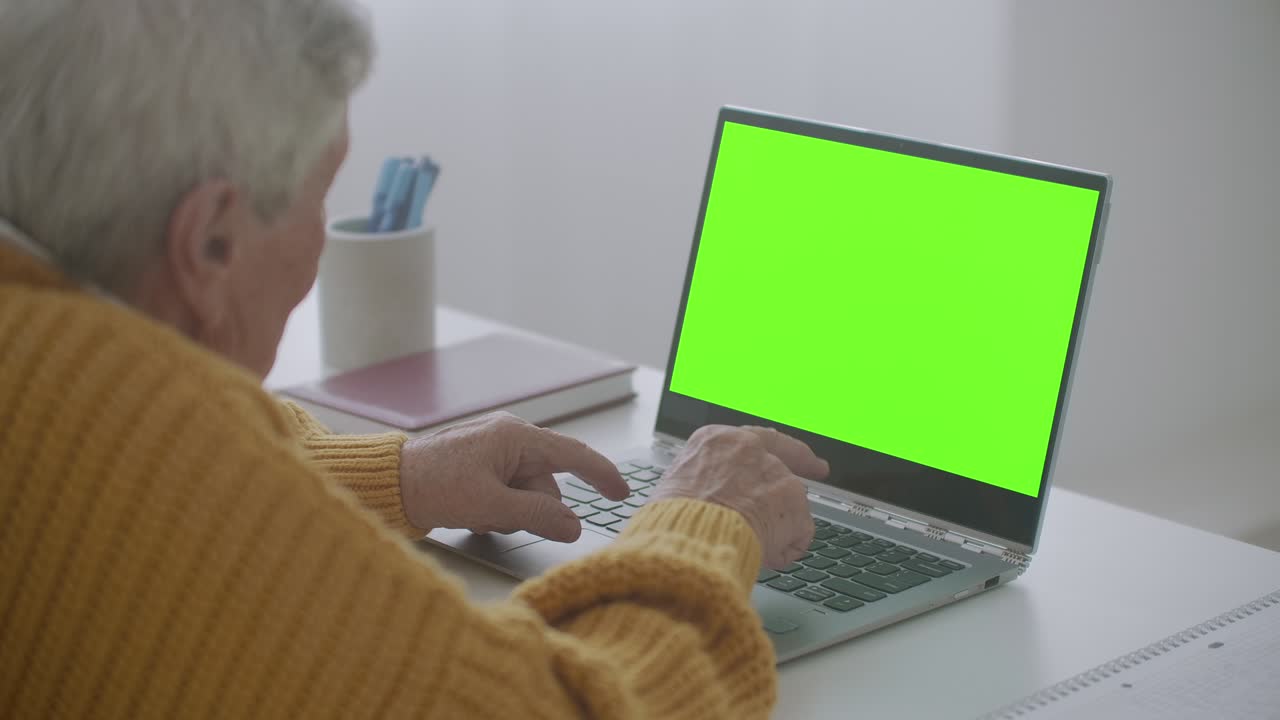 mujer madura asintiendo con la cabeza sí mientras mira una computadora de pantalla verde. mujer madura anciana con cabello gris y una videollamada en su computadora portátil. computadora portátil con pantalla verde